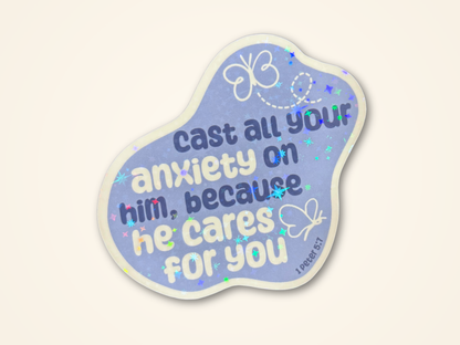 A sticker featuring the text 'cast all your anxiety on him, because he cares for you' in white and dark blue lettering. The sticker has a light blue-purple background with white doodles of butterflies and a holographic glitter texture, and is shown on a warm off-white background.