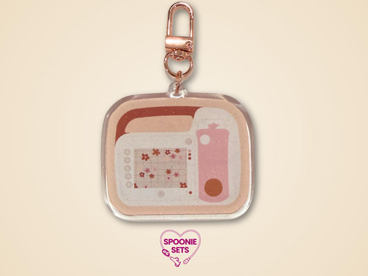 Keychain with a pink and beige feeding tube pump design with floral accents and rose gold hardware