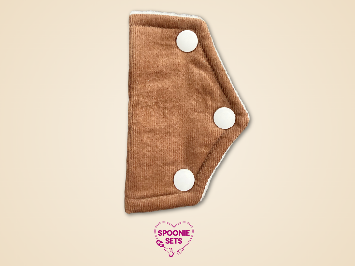 Brown cloth pad with white buttons on a beige background, featuring 'Spoonie Sets' logo.