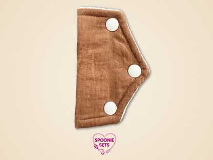 Brown cloth pad with white buttons on a beige background, featuring 'Spoonie Sets' logo.