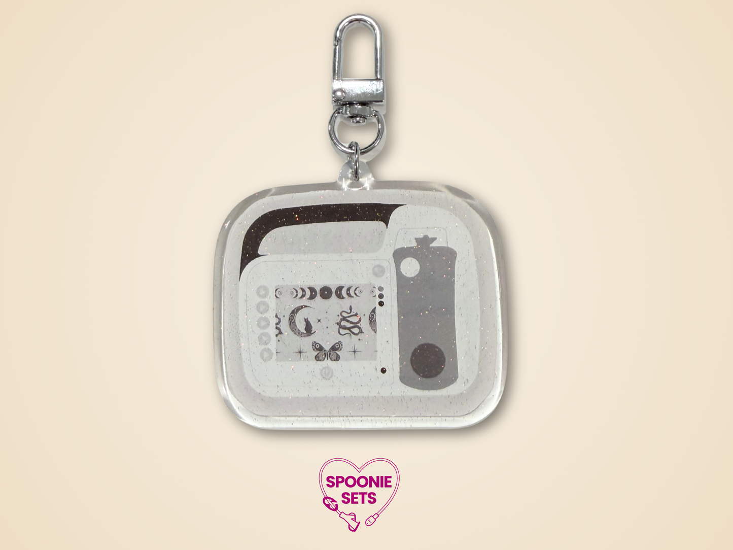 Keychain Side B with white, light gray, and dark gray feeding tube pump design with celestial accents and silver hardware
