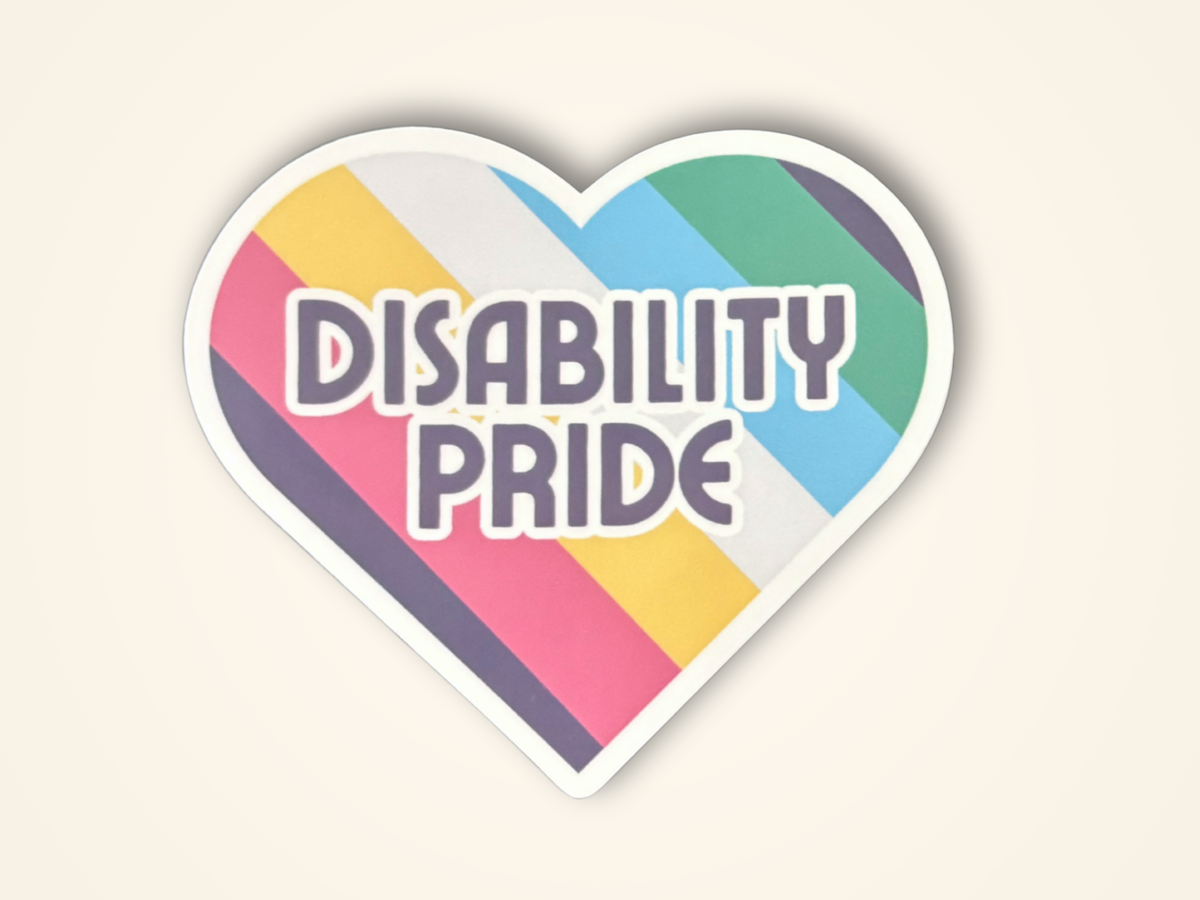 A heart-shaped sticker with the words 'DISABILITY PRIDE' in bold white letters, set against a background of diagonal multicolor stripes in red, yellow, white, blue, green, on a light beige background.
