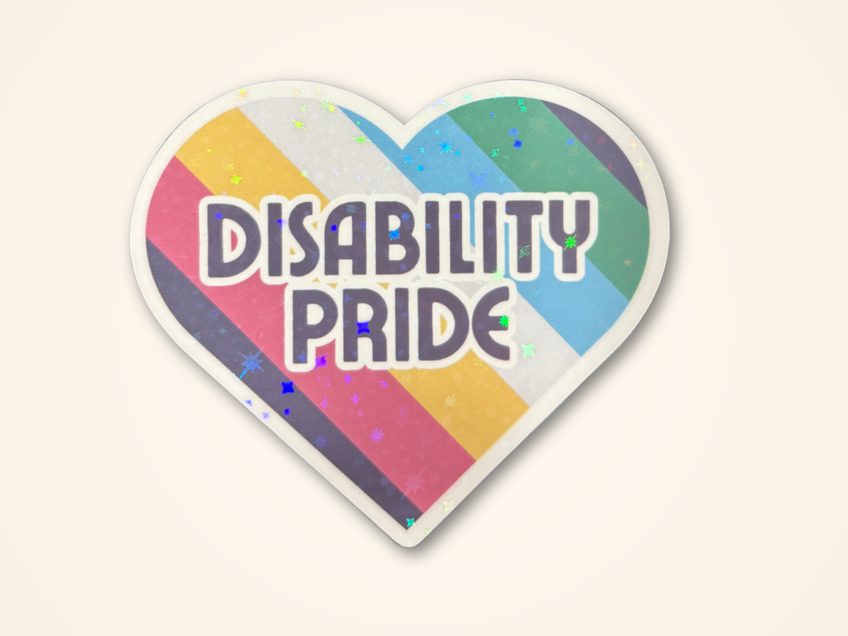 A heart-shaped sticker with the words 'DISABILITY PRIDE' in bold gray letters over a rainbow-striped background with subtle glitter, shown on a light cream background.