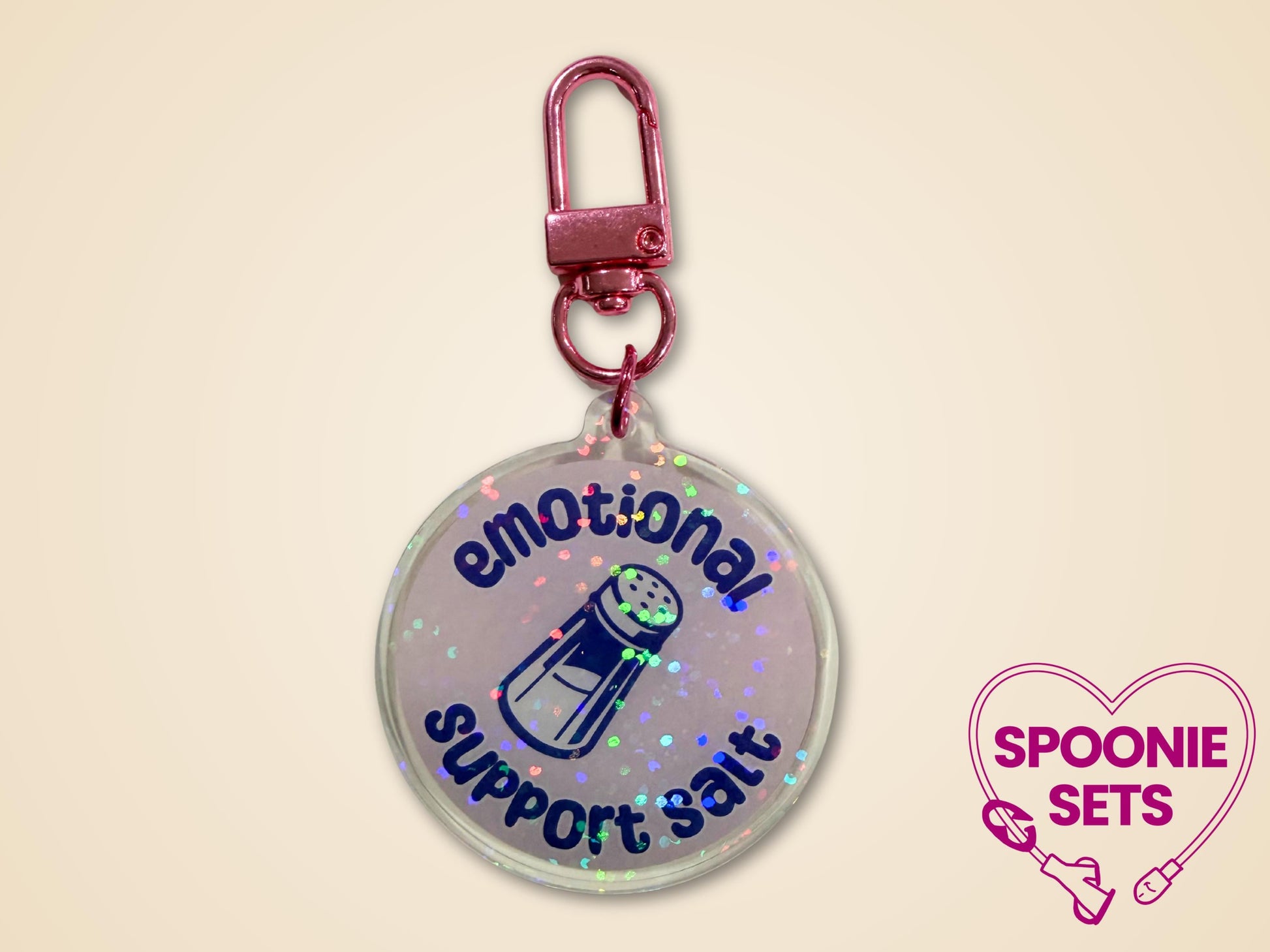 Holographic acrylic keychain with "Emotional Support Salt" text and a salt shaker design, attached to a pink clip.