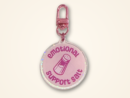 A round keychain with a metallic rose gold clasp, featuring the text 'emotional support salt' and a salt shaker illustration.