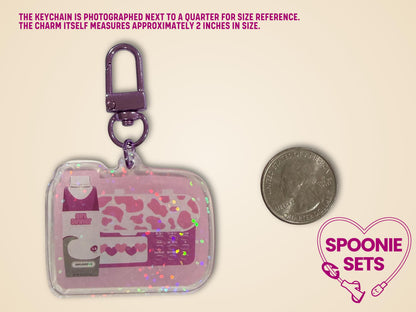 Pink "Girl Dinner" acrylic keychain with feeding tube pump and formula bottle design, holographic dot overlay, next to a quarter.