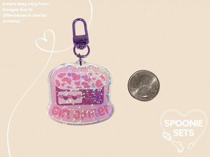 Pink acrylic keychain with a feeding tube pump design, "Girl Dinner" text, and holographic glitter.
