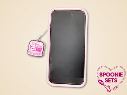Pink "Girl Dinner" feeding tube pump acrylic phone charm with glitter epoxy finish, attached to a phone.