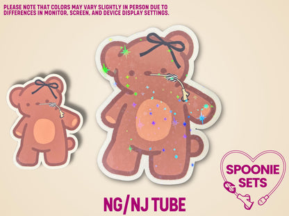 Two brown teddy bear stickers with black bows and feeding tubes, one small and one large with holographic glitter.